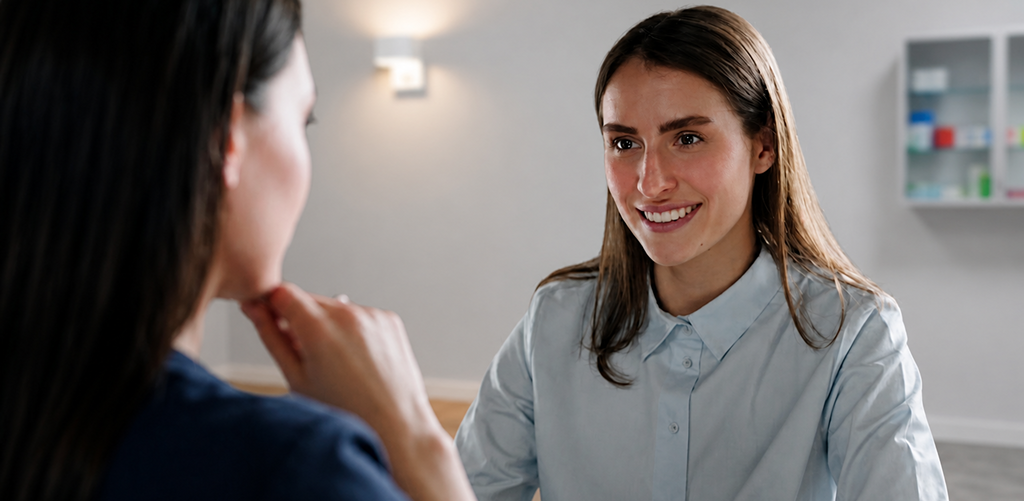 konsultacija A smiling woman in a light blue shirt talks with another person in a clinic-like office setting.